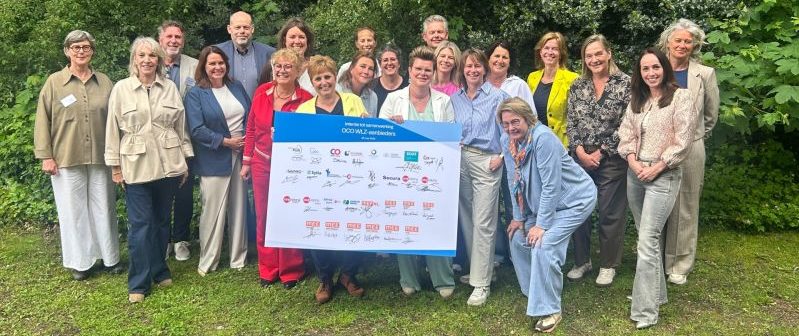 Een groep mensen achter een bord met logo's van de organisaties die de intentieverklaring hebben ondertekend.